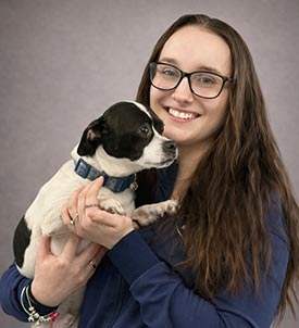 Sara posing for a picture with a dog on grey background